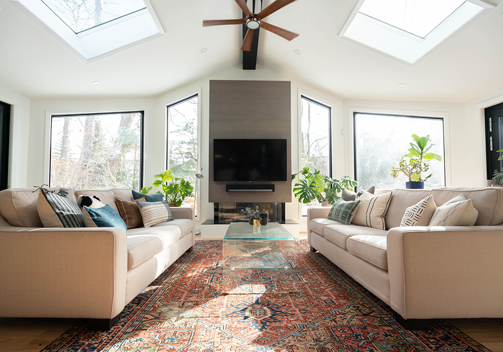 A clean interior space with two couches facing each other in a vaulted room with large windows and a celling fan.
