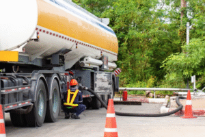 A worker using a fuel line connecting from a fuel truck to an underground fuel storage.