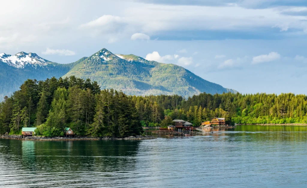 A scenic view over the Ocean towards several oceanfront homes with a snowcapped mountain range in the distance