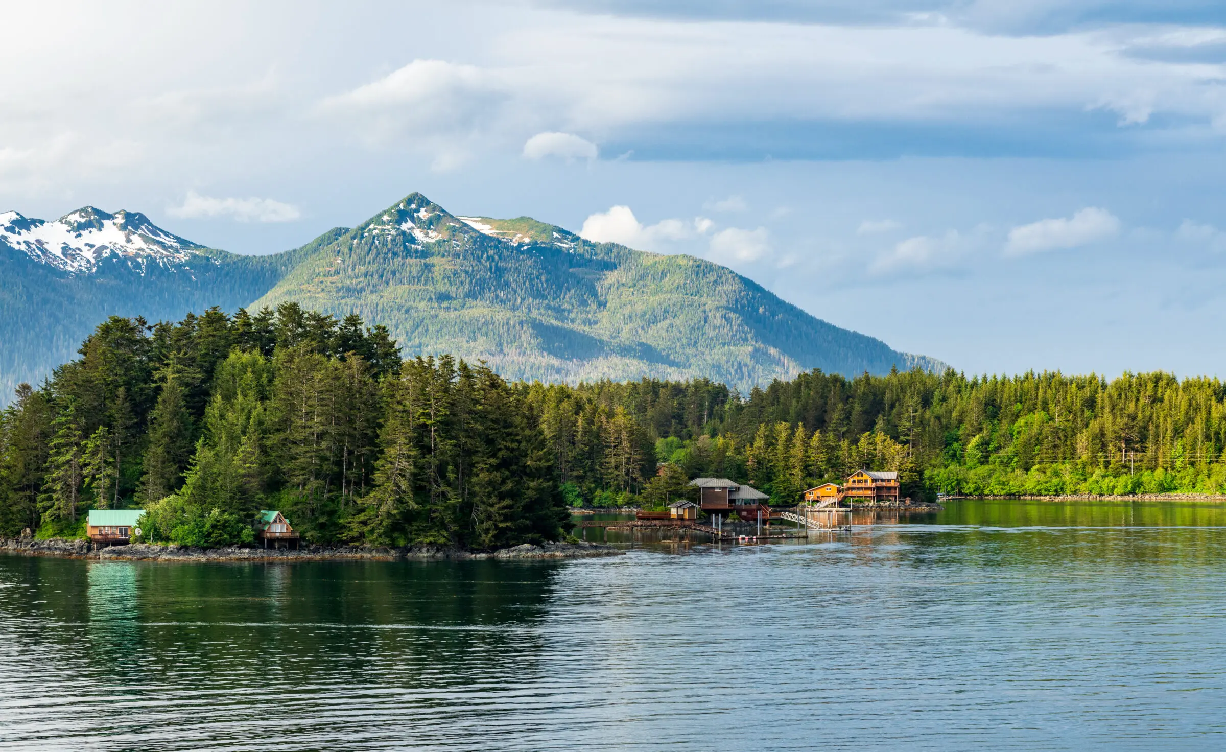 A scenic view over the Ocean towards several oceanfront homes with a snowcapped mountain range in the distance