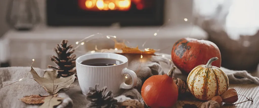 A well staged cozy environment with a cup and pumpkins around a fireplace